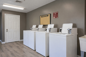 Three white washing machines are lined up in a laundry room.
